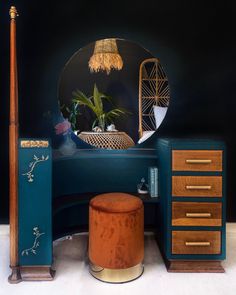 a desk with a mirror, stool and lamp on it in front of a black wall