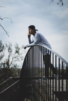 a man standing on top of a metal fence next to a tree and looking off into the distance