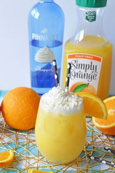 an orange drink with whipped cream garnish on the rim next to some oranges