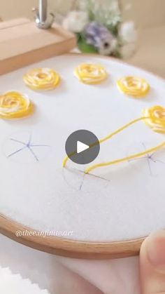 someone is stitching yellow flowers on a white piece of fabric with a wooden frame