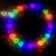 many hearts are arranged in the shape of a circle on a black background with bright lights