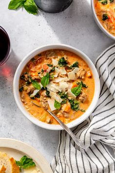 two bowls of soup on a table with bread, wine and basil leaves next to it