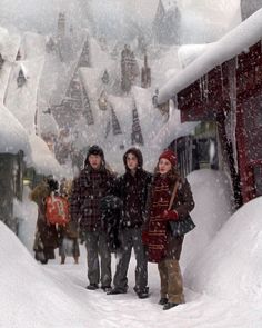 three people standing in the snow near a building