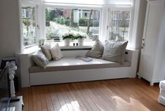 a window seat with pillows on it in front of a wooden floor and white walls