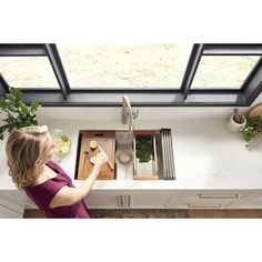 a woman standing in front of a kitchen sink with a cutting board on the counter