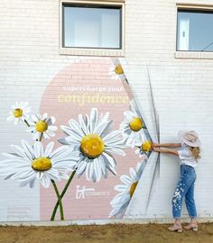 a woman standing in front of a wall with flowers painted on it and holding onto the side