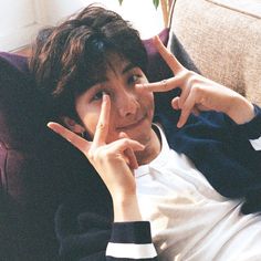 a young man sitting on top of a couch making the peace sign with his fingers