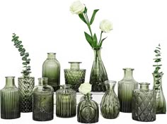 a collection of green vases and flowers on a white surface with greenery in them