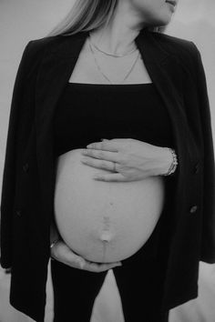 a pregnant woman is holding her belly in front of the camera while wearing a black jacket