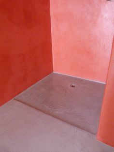 an empty bathroom with red walls and concrete floor