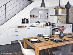 a table with place settings and plates on it in the middle of a kitchen area