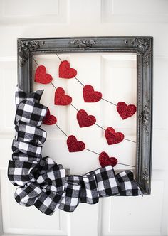 a frame with some hearts hanging on the front door and a bow attached to it