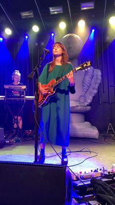 a woman standing in front of a microphone and guitar