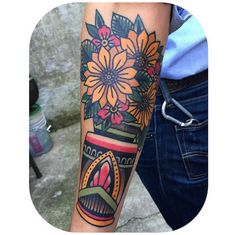 a person with a tattoo on their arm holding a cup and flowers in it's hand