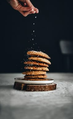 someone sprinkling sugar on top of a stack of pancakes