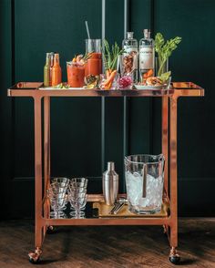 a bar cart filled with drinks and glasses on top of a wooden floor next to a green wall