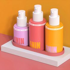 three different colored bottles are on a white shelf next to an orange and pink wall