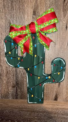 a painted cactus with christmas lights and a bow on it's head is sitting against a wooden wall