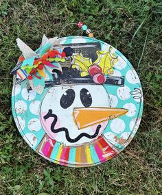 a paper plate with a painted snowman face on top of it sitting in the grass