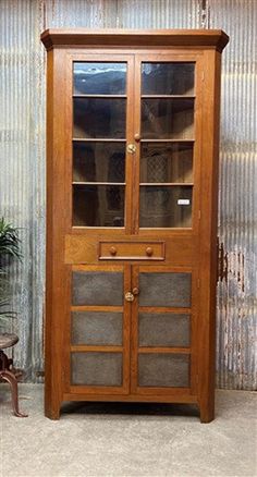 an old wooden cabinet with glass doors and drawers in front of a metal curtained wall