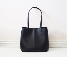 This simple tote features black vegan (fake) leather, magnet top closure and internal pockets. Details:-Dimensions: 12" length (top to bottom), 10" bottom width, 7" depth, 10" X 7" base (bottom)-Each shoulder strap measures approximately 23" full length-Black vegan (fake) leather-Fabric interior lining (solid black) - color can be customized-Internal pockets: 1 slip pocket, 1 zippered pocket-Magnet top closureBecause each bag is made by hand, the measurement is approximate and may vary slightly Minimalist Everyday Bags With Magnetic Closure, Sleek Everyday Bags With Magnetic Closure, Minimalist Black Hobo Bag For Office, Minimalist Black Bucket Shoulder Bag, Sleek Black Satchel For Everyday Use, Black Minimalist Bucket Shoulder Bag, Minimalist Shoulder Bag With Magnetic Closure For Daily Use, Minimalist Black Bucket Bag, Sleek Everyday Tote Shoulder Bag