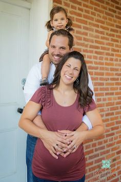 a man and woman are holding their daughter in front of a brick building with the door open