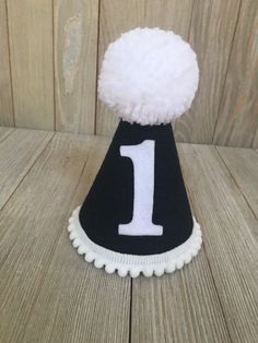 Please read shop announcement for current processing times and updates. Your birthday boy will look absolutely adorable in this mini birthday hat for his half birthday or whole birthday! Perfect for a party or photo shoot. This hat is available as a mini size (5 inches tall by 4 inches wide) Or a full size (7 inches tall by 5 inches wide). It features black felt with a white number of your choice. White mini pom pom ribbon is attached along the base of the hat with a yarn Pom Pom on top. It has White Fun Party Supplies For Birthday, Fun White Birthday Party Supplies, Fun White Party Supplies For Birthday, Cute White Hat For First Birthday, White Birthday Party Hat Supplies, Playful White Hat For First Birthday, Playful White Hat For Birthday, Playful White Hats For Birthday, Fun White Birthday Hat