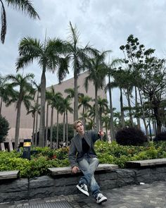 a man is sitting on a stone wall with palm trees in the background and he has his arms out