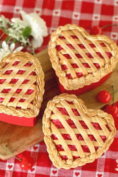 three heart shaped pies sitting on top of a cutting board next to cherries