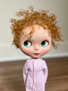 a doll with red hair and green eyes standing on a wooden floor in front of a white wall