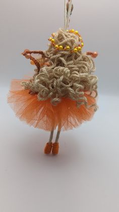 the doll is wearing an orange tutu skirt and holding a pair of knitting needles