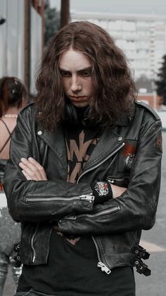 a man with long hair wearing a black leather jacket and holding his arms crossed in front of him