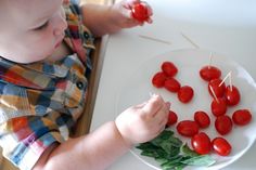 a toddler is playing with cherry tomatoes on a white plate while sitting at a table