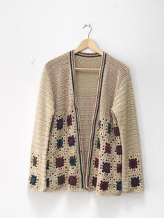 a crocheted cardigan sweater hanging on a hanger against a white wall