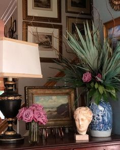 there is a vase with flowers in it on the table next to pictures and a lamp