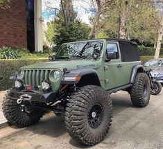 a green jeep parked in front of a building with two large tires on it's sides