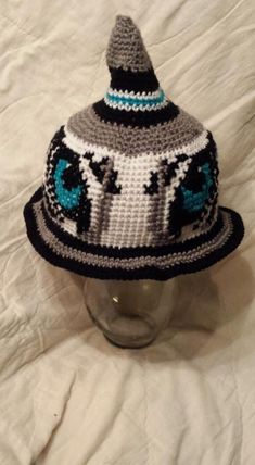 a crocheted hat sitting on top of a white bed next to a glass vase