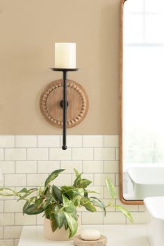 a candle is lit on the wall next to a potted plant in front of a mirror