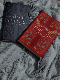 two books sitting on top of a bed next to each other in front of a gray blanket