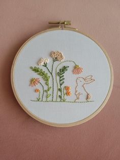 an embroidery project with flowers and a bunny in the grass, on a pink background