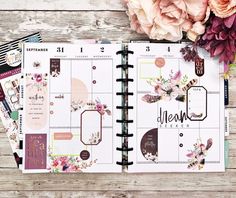 an open planner book sitting on top of a wooden table next to flowers and paper