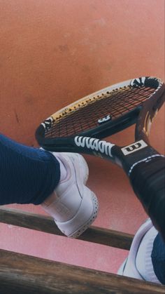 a person holding a tennis racquet on top of a wooden floor next to a pink wall