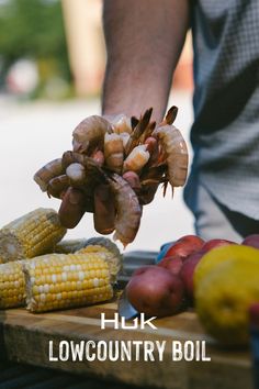 the man is preparing his food on the grill with shrimp, corn, and potatoes