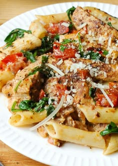 a white plate topped with pasta and meat covered in sauce on top of a wooden table