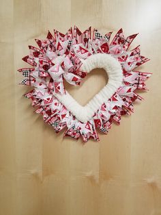 a heart - shaped wreath made out of red and white paper on a wooden surface