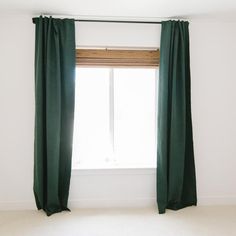 a green curtain hanging in front of a window with white walls and carpeted floor