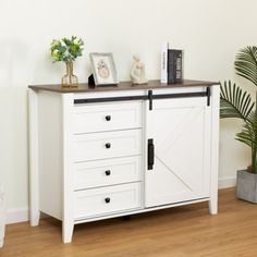 a white cabinet with doors and drawers in a room next to a potted plant