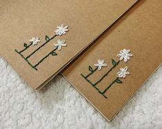 two brown notebooks with white flowers on them sitting on a bed next to each other