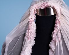 a white veil with pink beading on top of a mannequin headpiece