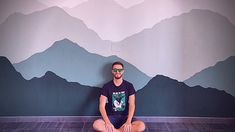 a man sitting on the floor in front of a wall with mountains painted on it